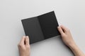 Black A6 Bi-Fold / Half-Fold Brochure Mock-Up - Male hands holding a black bi-fold on a gray background