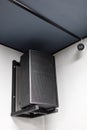 Black big musical powerful speaker with protective grill hanging on wall in public place.