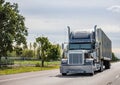 Black big rig classic semi truck with chrome accessories transporting cargo in long industrial container running on the straight Royalty Free Stock Photo