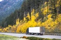 Black big rig long hauler semi truck transporting cargo in reefer semi trailer driving on the highway road with yellow autumn Royalty Free Stock Photo