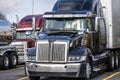 Black big rig modern semi truck with semi trailer standing on truck stop with another semi trucks Royalty Free Stock Photo