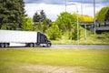 Black big rig semi truck with dry van semi trailer going to highway on the intersection with traffic light and over pass road