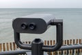 Black binoculars on swivel hinge on the observation deck on the sea embankment, directed slightly to right on azure sea horizon