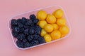 Black blackberries and yellow plums in an open plastic box