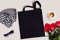 Black blank cotton eco tote bag with red roses, glasses, scarf and a cup of coffee, styled design mockup Royalty Free Stock Photo