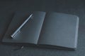 Black blank notebook or plain notepad or diary or journal for writing text and message with pen on table or desk as background