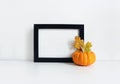 Black blank wooden frame mockup with an orange pumpkin and golden oak leaves lying on the white table. Poster product Royalty Free Stock Photo