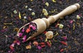 Black blended tea with flower petals and dried fruit on a wooden spoon. close up Royalty Free Stock Photo