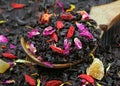 Black blended tea with flower petals and dried fruit on a wooden spoon. close up Royalty Free Stock Photo