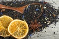 Black blended tea with flower petals and dried fruit in wooden spoon on wooden desk. Black tea and dried oranges Royalty Free Stock Photo
