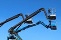 Black and blue aerial work platforms of cherry picker against blue sky