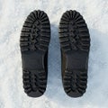 Black boot soles with a rugged tread pattern are placed on snowy ground. The design Royalty Free Stock Photo