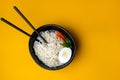 Black bowl of chineese fast cooked noodle with egg and vegetables. Black chopsticks near it at yellow background.