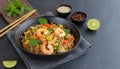 In a black bowl, noodles, veggies, and prawns are stir-fried. slate background. higher perspective