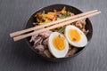 Black bowl of ramen noodles with boiled eggs, veggies and turkey meet, ready to be poured with boiling broth. Wooden