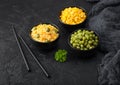 Black bowls with boiled organic basmati vegetable rice, yellow corn and peas with black chopsticks on black stone background with