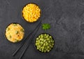 Black bowls with boiled organic basmati vegetable rice, yellow corn and peas with black chopsticks on black stone background. Top