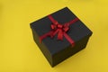 Black box with red bow on yellow background. Gift wrapping Royalty Free Stock Photo