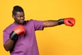 Black boxer guy throwing punch wearing boxing gloves, yellow background Royalty Free Stock Photo