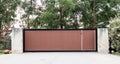 Black brown metal wrought iron driveway property entrance gates set in concrete brick fence, lights, eucalyptus garden trees in ba