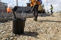 A black bucket with liquid bitumen and a worker with a shovel during road works, landscaping and laying out asphalt on a city