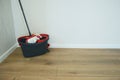 Cleaning mop and black bucket with wringer on wooden floor near white wall. Accessories for cleaning home and office Royalty Free Stock Photo