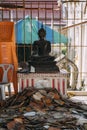 Black buddha statue sitting behind pile of roof tiles in temple being renovated