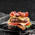 Black burger with beaf steak, lettuce, tomatoes, slice of cheese, ham, pastrami and sauce on slate black background, close up Royalty Free Stock Photo