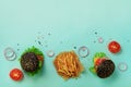 Black burger, french fries potatoes, tomatoes, cheese, onion, cucumber and lettuce on blue background. Top view. Fast food banner Royalty Free Stock Photo