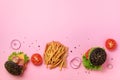 Black burger, french fries potatoes, tomatoes, cheese, onion, cucumber and lettuce on pink background. Top view. Fast food banner