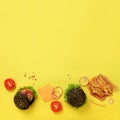 Black burger, french fries potatoes, tomatoes, cheese, onion, cucumber and lettuce on yellow background. Square crop. Top view. Royalty Free Stock Photo