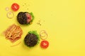 Black burger, french fries potatoes, tomatoes, cheese, onion, cucumber and lettuce on yellow background. Top view. Fast food Royalty Free Stock Photo