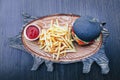 Black burger with French fries and sauce on a wooden board Royalty Free Stock Photo