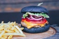 Black burger with French fries and sauce on a wooden board Royalty Free Stock Photo