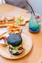 Black burger with meat patty, cheese, tomatoes, mayonnaise, french fries in a paper cup and glass of cold cola soda with ice.