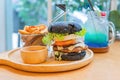 Black burger with meat patty, cheese, tomatoes, mayonnaise, french fries in a paper cup and glass of cold cola soda with ice.