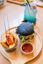 Black burger with meat patty, cheese, tomatoes, mayonnaise, french fries in a paper cup and glass of cold cola soda