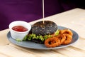 Black burger with meat tomato sause and potato rings on the wooden table