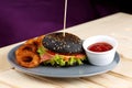 Black burger with meat tomato sause and potato rings on the wooden table