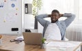 Black businessman leaning back on chair in office after successful work