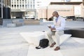 Black businessman sitting on the street with his work tools. He is wearing a medical mask