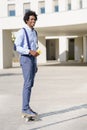 Black businessman on a skateboard holding a smartphone outdoors.