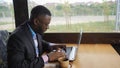 Black businessman is working typing a message on laptop sitting in summer cafe. Royalty Free Stock Photo