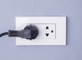 Black cable plugged in a white electric outlet mounted on gray w Royalty Free Stock Photo