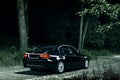 Black car BMW E90 stand on road in darkness forest at night