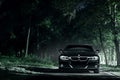 Black car BMW E90 stand on road in darkness forest at night