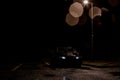 A black car with headlights on, under a street light on a dark wet moody night