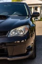 Black car in static on a sunny day. Front view half of the car -hood, headlight and a wheel. Vertical orientation. Royalty Free Stock Photo