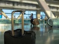 Black carry on luggage sitting at modern airport with workers in Royalty Free Stock Photo