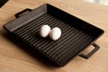 Black cast heavy iron grill pan in two organic white eggs; on modern oak kitchen countertop